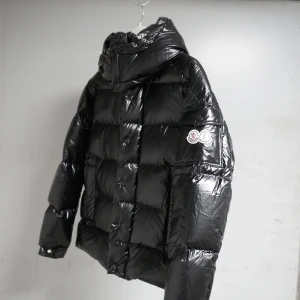 Svart glansig dunjacka från Moncler Maya 70 - Säljer en svart glansig dunjacka från Moncler med huva och dragkedja. Jackan har ett quiltat mönster och Moncler-logga på ärmen. Perfekt för kalla dagar med sin varma och stiliga design. Size 1. 