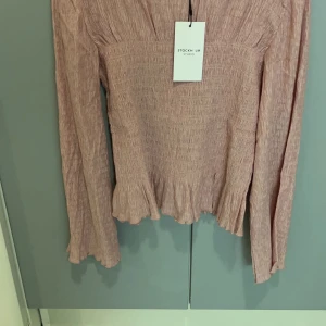 Rosa långärmad topp från Stockh LM Studio - Säljer en söt rosa långärmad topp från Stockh LM Studio. Toppen har en smockad design som ger en fin textur och en lätt volangdetalj vid nederkanten. Perfekt för en stilren och bekväm look.