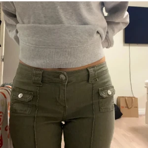 Olivgröna utsvängda byxor - Snygga olivgröna byxor med praktiska fickor och knappar framtill. Byxorna har en bootcut-stil och är lågmidjade, vilket ger en smickrande passform. Perfekta för en avslappnad look.