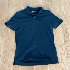 Mörkblå pikétröja  - Snygg mörkblå pikétröja från Dressmann. Korta ärmar och krage med knappar.