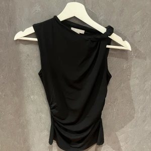 Svart ärmlös topp från H&M - Snygg svart ärmlös topp från H&M med en elegant drapering och knutdetalj vid axeln. 