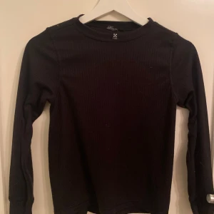Svart ribbad tröja från X-Trail - Säljer en svart ribbad tröja från X-Trail. Tröjan har långa ärmar och en enkel design som passar perfekt för kyligare dagar. Perfekt för dig som gillar en stilren look.