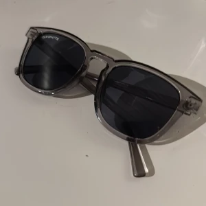 Grå solglasögon från Granite - Snygga solglasögon från Granite med transparent grå båge och mörka linser. Perfekt för en stilren look. De har en klassisk form som alltid går hem. Dock är dom lite snea men inget man märker av så mycket! De är knappast använda men pga att de är lite snea så påverkar de skicket mycket, annars skick 10/10! Frakt ingår inte!