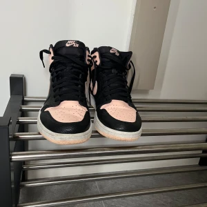 Nike Air Jordans i svart och rosa - Snygga Nike Air Jordans i en cool kombination av svart och rosa. Skorna har en klassisk hög design med snörning och den ikoniska Nike-loggan på sidan. Perfekta för dig som vill ha en stilren och sportig look.