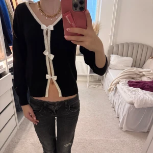 Svart kofta med vita rosetter🎀🎀🎀 - Säljer en svart kofta med vita detaljer och tre söta rosetter framtill. SUPER söt 🎀🎀🎀🎀