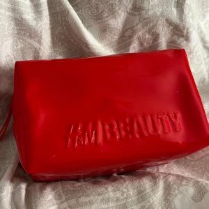 Röd necessär från H&M Beauty - Snygg och praktisk röd necessär från H&M Beauty. Tillverkad i glansigt syntetmaterial med präglad logga på framsidan. Perfekt för att förvara smink och andra skönhetsprodukter. Stängs med dragkedja för säker förvaring.