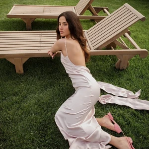 Ljusrosa långklänning med öppen rygg - Elegant ljusrosa långklänning i satin med smala axelband och en vacker öppen rygg. Klänningen har en slits baktill för extra rörelsefrihet och en figurnära passform som framhäver silhuetten. Perfekt för speciella tillfällen.