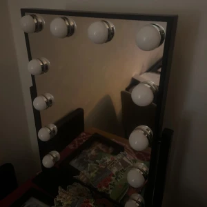 Sminkspegel med lampor - Snygg sminkspegel med inbyggda lampor runt kanterna. Perfekt för att få bra belysning vid sminkning eller styling. Spegeln passar bra på sminkbordet eller i sovrummet. Finns 3 olika ljuslägen, sladd. Har storlek 30x40. Köpt på Rusta för 500, säljer för 300. Använd 1-2 gånger..