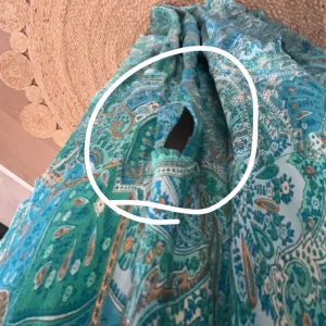 Turkos mönstrad kjol - Säljer en turkos kjol med ett vackert paisleymönster i gröna och blå nyanser. Kjolen har en elastisk midja för bekväm passform och är perfekt för sommarens varma dagar. Den är lätt och fladdrig, vilket ger en härlig känsla när du rör dig. Passar perfekt till en enkel topp eller blus. Det är även ett hål i den men är lätt att sy men det syns ej tydligt, pris kan diskuteras!