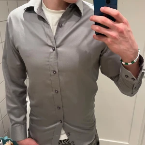 Silke skjorta från Bellissimo - Snygg grå skjorta från Bellissimo i silke. Skjortan har långa ärmar och knappar framtill. Perfekt för en stilren look. Jag är 190 cm och den sitter lite tajt på mig 