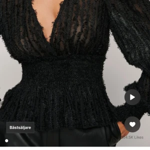 Svart blus med volangdetaljer - Elegant svart blus med djup v-ringning och volangdetaljer. Blusen har långa ärmar och en smickrande passform med markerad midja. Perfekt för en stilfull look. Skriv för bild på min tröja. 