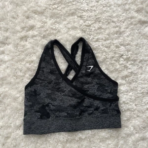 Grå camotopp från gymshark stl S - Säljer en grå sporttopp från Gymshark med ett snyggt kamouflagemönster stl S. Toppen har korsade axelband använt skick lite nopprig vid axlarna, inlägg medföljer inte, köparen betalar frakt☺️