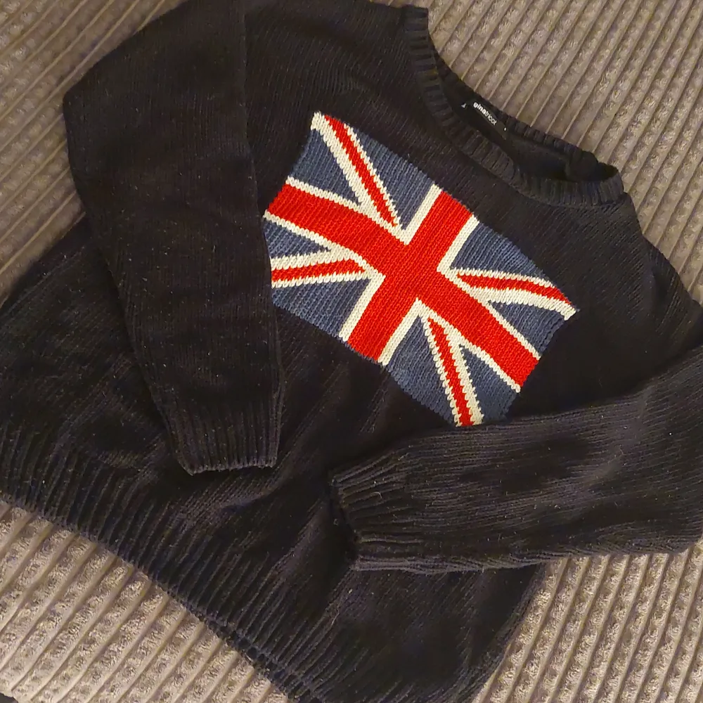 Säljer en cool svart stickad tröja från Gina Tricot med Union Jack-mönster på framsidan. Tröjan har långa ärmar och är perfekt för höst och vinter. Den är i storlek S och i bra skick. Perfekt för dig som vill ha en unik och stilren look!. Tröjor & Koftor.