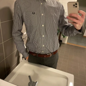 Fred perry svart-vit-rutig skjorta - strl L - Hej! Tänkte göra mig av med denna häftiga skjorta från brittiska Fred perry.  Materialet andas och känns skönt mot huden! Klassisk tidlös design med rutigt mönster.  Defekt: en knapp i ena ärmen som är halv, syns på bild