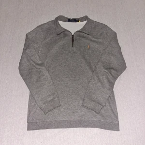 Polo Ralph Lauren Half zip Grå - Snygg grå tröja från Polo Ralph Lauren med dragkedja och broderad logga på bröstet. Perfekt för en stilren och avslappnad look. Tröjan har långa ärmar och en bekväm passform.