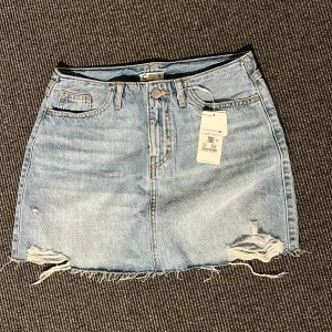 Blå jeanskjol - Snygg blå jeanskjol med slitna detaljer och fransig nederkant. Kjolen har klassisk femficksdesign och knappstängning fram. Perfekt för en avslappnad stil. Den är inte använd och har prislapp kvar, originalpris 299kr💛😍🥰