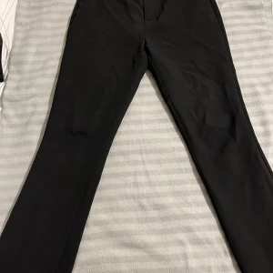 Svarta kostymbyxor från Gina Tricot - Snygga svarta kostymbyxor från Gina Tricot med dragkedja och knapp framtill. Perfekta för en stilren look. Storlek 36 