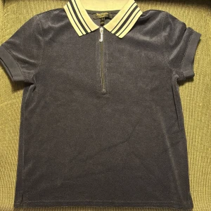 Mörkblå polotopp från Juicy Couture - Snygg mörkblå polotopp från Juicy Couture med dragkedja framtill. Kragen är vit med mörkblå ränder och har texten 'Juicy' broderad på baksidan. Säljer pga använd max tre gånger, har inte haft många tillfällen att ha den på mig! :,) OBS! Har hund i hemmet men hon fäller INTE päls!