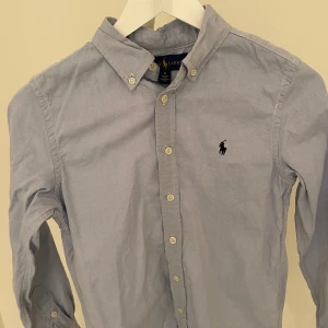 Blå skjorta från Ralph Lauren - Säljer nu min Ralph Lauren skjorta. Den är i mycket bra skick utan några defekter. Nypris: ca 1500. Mitt pris: 399. Hör av dig vid minsta fundering! Strl: 14 (barnstorlek).
