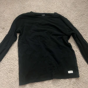 Svart långärmad tröja från Denim Makers - Snygg svart långärmad tröja från 157 Denim Makers. Perfekt för en stilren och enkel look. Tröjan har en liten etikett nertill som ger en diskret detalj.