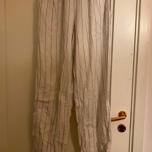 Randiga vita byxor - Säljer ett par vita byxor med svarta ränder. Byxorna har en loose passform och är högmidjade med elastisk midja för extra komfort. Perfekta för en avslappnad stil.                     Ska vara ett band rund midjan men har tappat de…