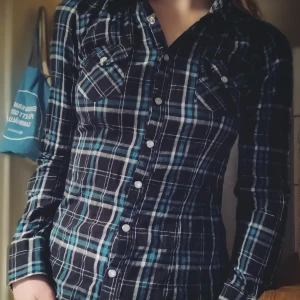 Rutig skjorta med knappar - Snygg rutig skjorta i grönt, blått och vitt med långa ärmar och knappar framtill. Perfekt för en avslappnad stil.