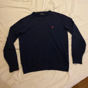 Mörkblå tröja från Ralph Lauren - Säljer en stilren mörkblå tröja från Ralph Lauren med det klassiska röda logotypbroderiet på bröstet. Tröjan har långa ärmar och en rund halsringning.
