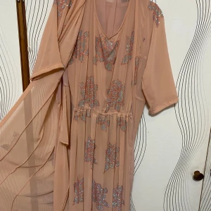 Beige klänning med glittrigt mönster - Elegant beige klänning med glittrigt mönster och v-ringad hals. Klänningen har kortärmade ärmar och en lös passform, perfekt för festliga tillfällen. Har använt den en gång och de va på ett bröllop