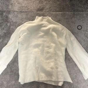 Vit stickad polotröja - Mysig vit stickad polotröja med långa ärmar och ribbade detaljer vid ärmslut och nederkant. Perfekt för kyliga dagar.