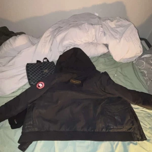 Svart dunjacka från Canada Goose - Säljer en svart dunjacka från Canada Goose med huva och dragkedja. Jackan har en broderad logotyp på ärmen och flera praktiska fickor framtill. Perfekt för kalla vinterdagar.  OBS!! Pris går att diskutera vid snabb affär