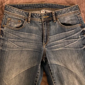 Blå jeans från Crystal Apparel - Snygga blå jeans från Crystal Apparel med klassisk femficksdesign och dragkedja. De har en lätt slitning för en trendig look och är perfekta för vardagsbruk. Passformen är straight och de är low waist.💕 Perfekta i skick förutom att det saknas en knapp, vilket enkelt går att fixa 😊.                                      Midja - 39 cm Inneben - 86 cm 