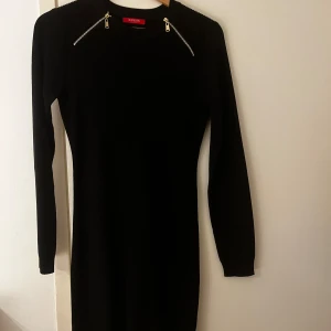 Svart klänning från Guess - Snygg svart klänning från Guess med långa ärmar och dragkedjedetaljer vid axlarna. Perfekt för en stilren look.