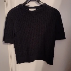 Svart stickad tröja från Kappahl - Säljer en snygg svart stickad tröja från Kappahl i storlek S. Tröjan har ett fint mönster och korta ärmar, perfekt för en stilren look. Passar bra till både jeans och kjol.