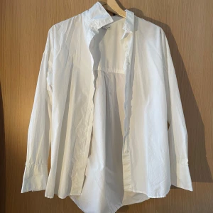 Vit skjorta i ekologisk bomull - Säljer en stilren vit skjorta i ekologisk bomull från märket C. Skjortan har långa ärmar och knappar framtill. Perfekt för en klassisk look.