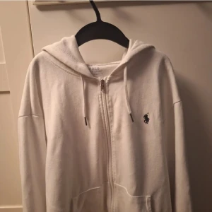 Vit hoodie från Polo Ralph Lauren - Säljer en stilren vit hoodie från Polo Ralph Lauren med dragkedja och det klassiska logotypbroderiet på bröstet. Perfekt för en avslappnad och snygg look.