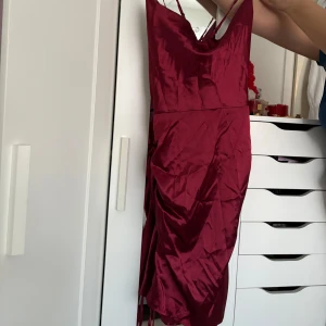 Vinröd sidenklänning - Snygg vinröd klänning i siden med smala axelband och en elegant drapering. Perfekt för en festlig kväll eller speciellt tillfälle.