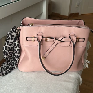 Rosa handväska med leoparddetalj - Snygg rosa handväska i syntetmaterial med guldfärgade detaljer och en dekorativ knytning framtill. Skitsnygg men säljer då den ej kommer till användning!💗