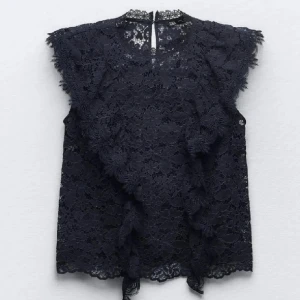 Spetsblus - Elegant marinblå spetsblus med vackra volangdetaljer. Blusen är ärmlös och har en rund halsringning. Perfekt för en stilfull look.