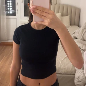 Svart ribbad kortärmad topp - Säljer en stilren svart ribbad topp med korta ärmar. Perfekt för en casual look eller att matcha med olika outfits. Toppen har en tight passform och är croppad för en modern stil.