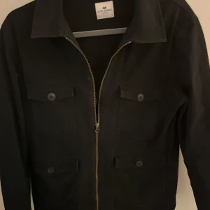 Svart overahirt från John Henric - Snygg svart jacka från John Henric med dragkedja och knappar på fickorna. Grymt skick fortfarande 9/10. Pris 799 kr 