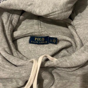 Grå hoodie från Polo Ralph Lauren - Säljer en grå hoodie från Polo Ralph Lauren åt min kille. Logotypen på bröstet är mörkblå. Nypris 2199kr, säljer för 549kr. Den är använd men i bra skick. Storlek L.