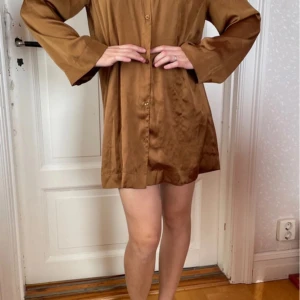 Brun skjortklänning - Säljer en snygg brun skjortklänning i mycket bra skick. Den har en avslappnad passform med långa ärmar och knappar framtill. Perfekt för höst och vår, och kan stylas både upp och ner beroende på tillfälle. Som jul, nyår och andra fester. Materialet känns mjukt och bekvämt mot huden.