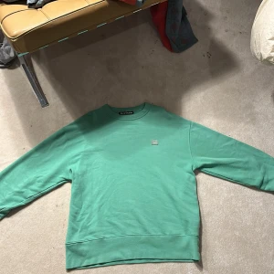 Grön sweatshirt från Acne Studios - Säljer en snygg grön sweatshirt från Acne Studios i väldigt bra skick. Den har en enkel design med en liten logga framtill. Perfekt för en avslappnad stil och passar till alla årstider. Skön och stilren, ett måste i garderoben! Nypris omkring 3000 mitt pris 399