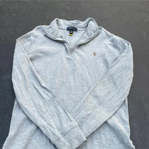 En half zip Polo Ralph Lauren - Säljer en stilren grå tröja från Polo Ralph Lauren. Den har en halv dragkedja och ett litet broderat märke på bröstet. Perfekt för både vardag och lite finare tillfällen. Tröjan är i mycket bra skick och passar perfekt till höst och vår.