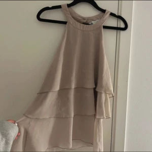 Beige ärmlös topp - Säljer en superfin beige topp med volanger. Den är ärmlös och har en luftig passform. Materialet känns mjukt och bekvämt mot huden. Passar både till vardags och festligare tillfällen. 🥰