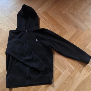 Svart, hel-zip hoodie från Ralph Lauren - Säljer en snygg svart hoodie från Ralph Lauren. Den har en dragkedja framtill och den klassiska broderade loggan på bröstet. Perfekt för både höst och vår. Den är i acceptabelt skick men har tröttnat på den. Om ni behöver fler bilder så säg till. 🤝🤝
