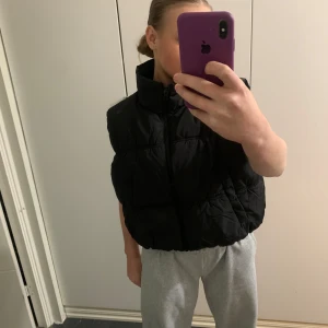 Svart dunväst med dragkedja - Säljer en svart dunväst i storlek dam L. Västen har en hög krage och stängs med dragkedja framtill. Perfekt för höst och vår när du vill hålla dig varm men ändå se stilren ut. Passar bra till både vardag och festliga tillfällen. Har aldrig använd den eftersom köpte i fel storlek (oanvänd) 