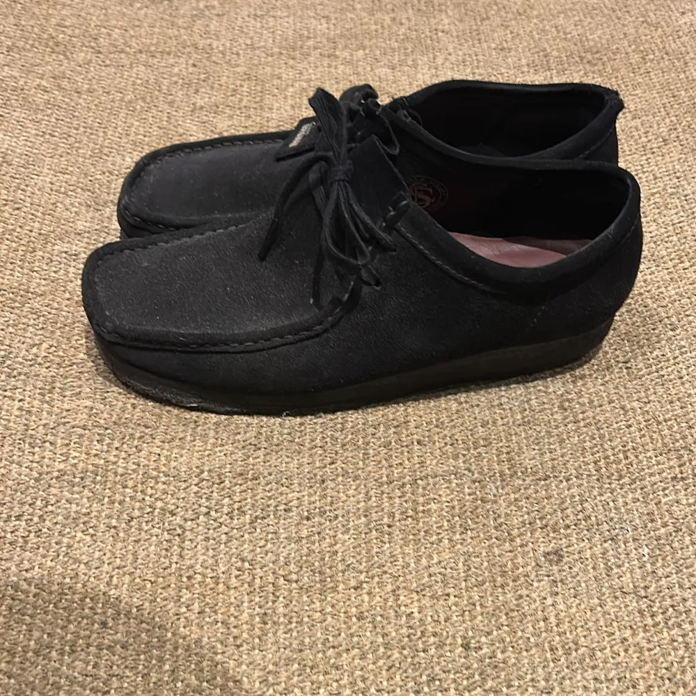 Säljer ett par snygga svarta mockaskor från Clarks i bra skick. De har en klassisk design med snörning och en bekväm sula. Perfekta för både vardag och lite finare tillfällen. Skorna är i storlek herr 44.. Skor.