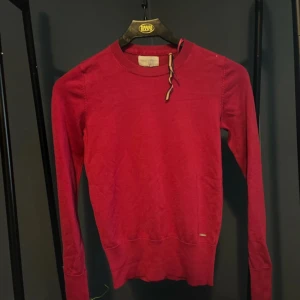 Röd tröja från Holly & Whyte - Säljer en snygg röd tröja från Holly & Whyte i storlek XS. Tröjan har långa ärmar och stilrena knappar vid ärmsluten. Perfekt för både vardag och fest! 💃