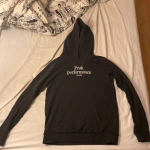 Svart hoodie från Peak Performance - Säljer en svart hoodie från Peak Performance i bra skick. Den har en klassisk design med logga på bröstet och en stor ficka framtill. Perfekt för höst och vinter när du vill hålla dig varm och bekväm. Passar både till vardags och träning. Storlek 170cm.